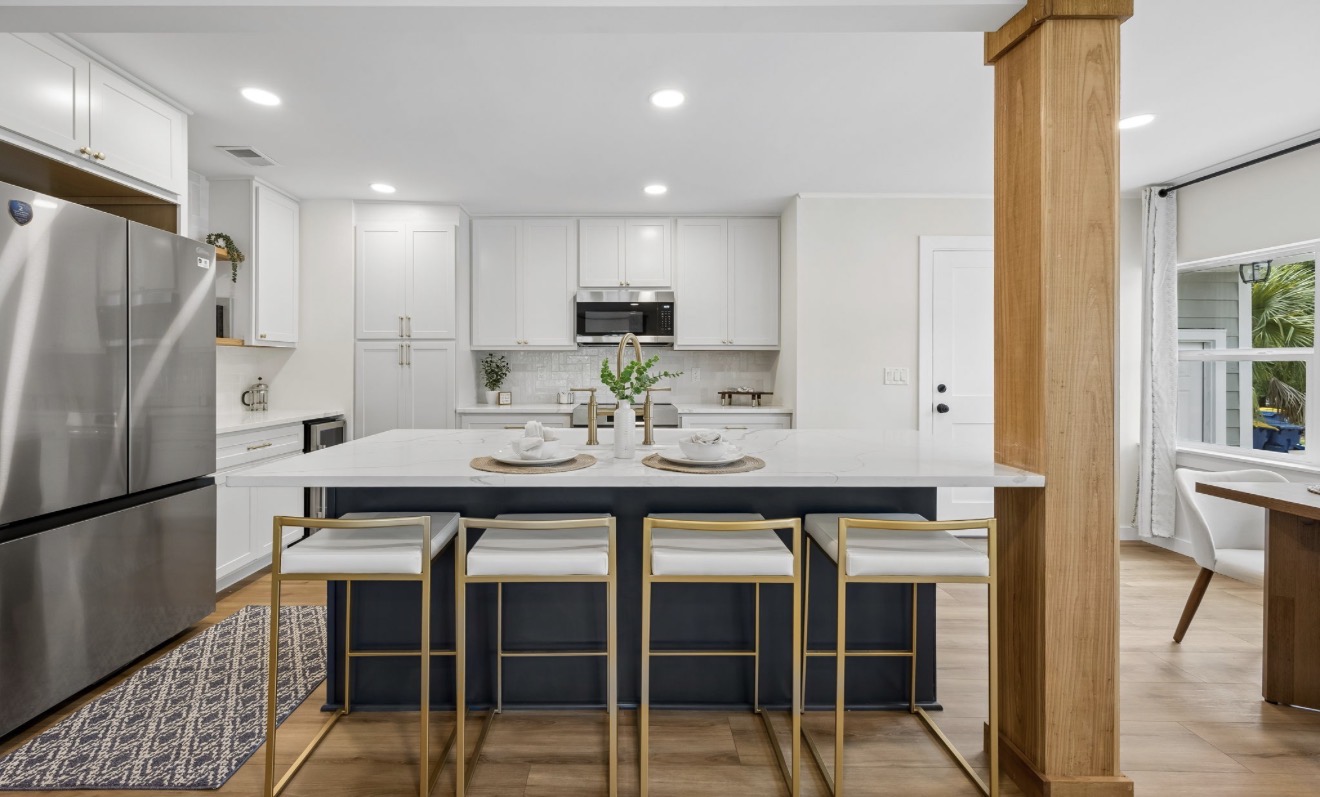 White kitchen with navy island, quartz waterfall counter, and brass barstools