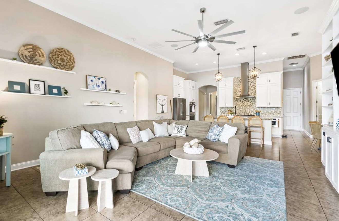 Open living room staged with a taupe sectional, coastal blue rug, and floating shelves at Ocean Breeze